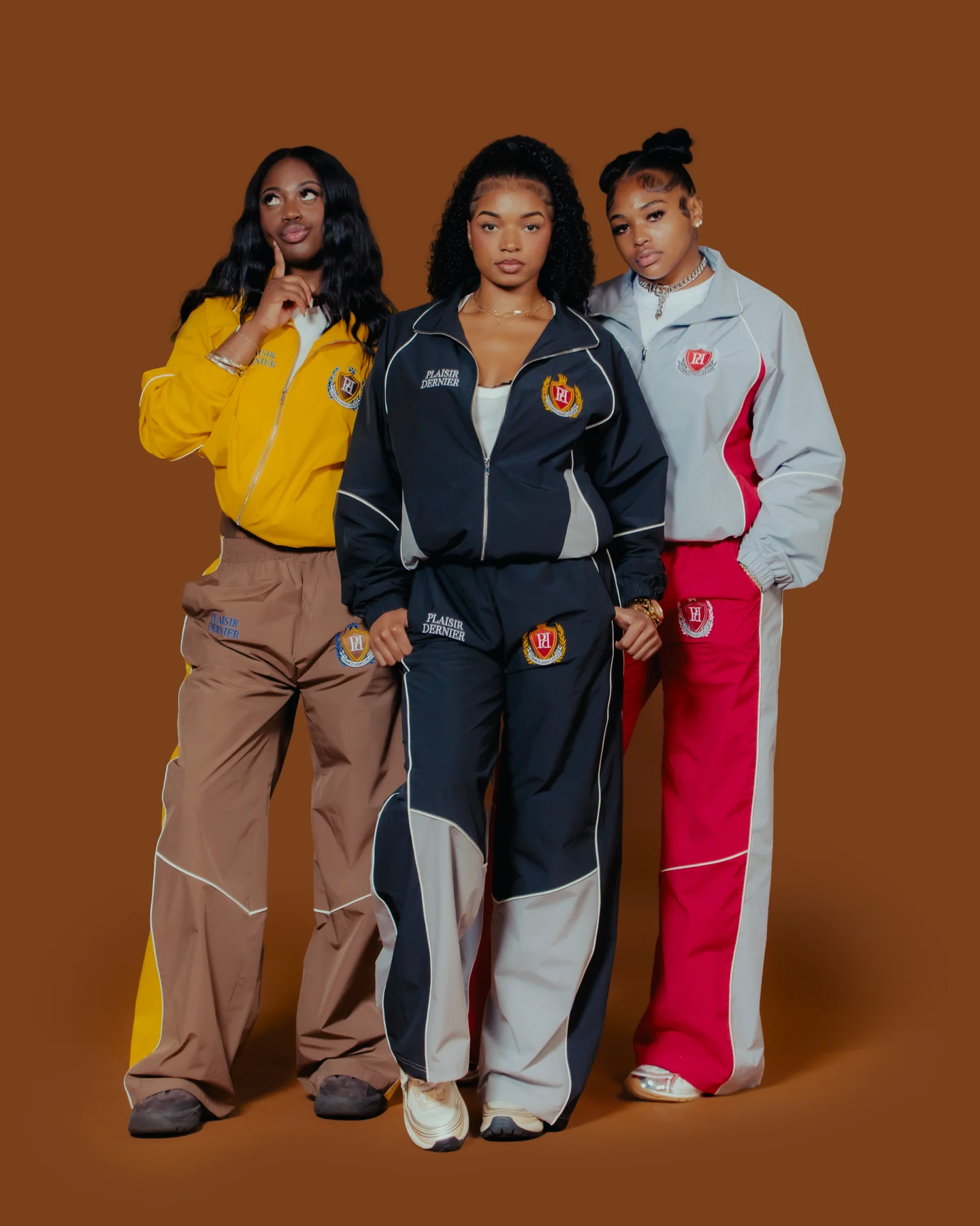 Three models wearing gold, midnight, and gray track sets against a warm studio backdrop